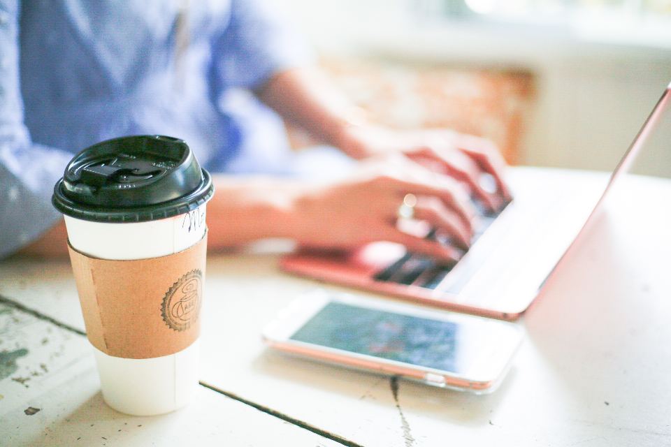 Hands typing on a laptop beside a cup of coffee